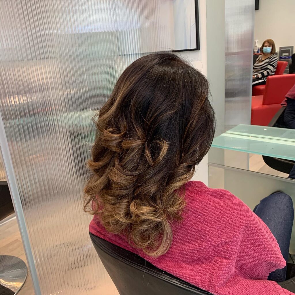Balayage caramel sur cheveux bruns bouclés, offrant volume et éclat dans un salon de coiffure professionnel.