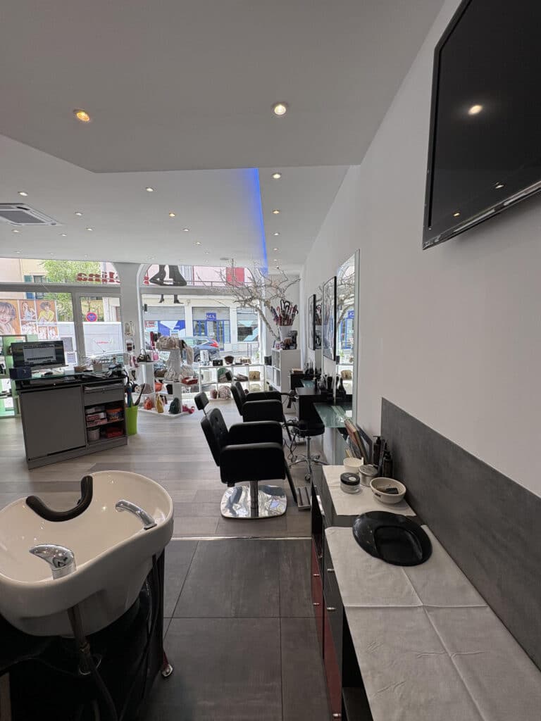 Salon de Coiffure Moderne : Intérieur et Équipement Salon de coiffure moderne avec bac à shampooing blanc, fauteuils noirs ergonomiques et grandes vitrines lumineuses.