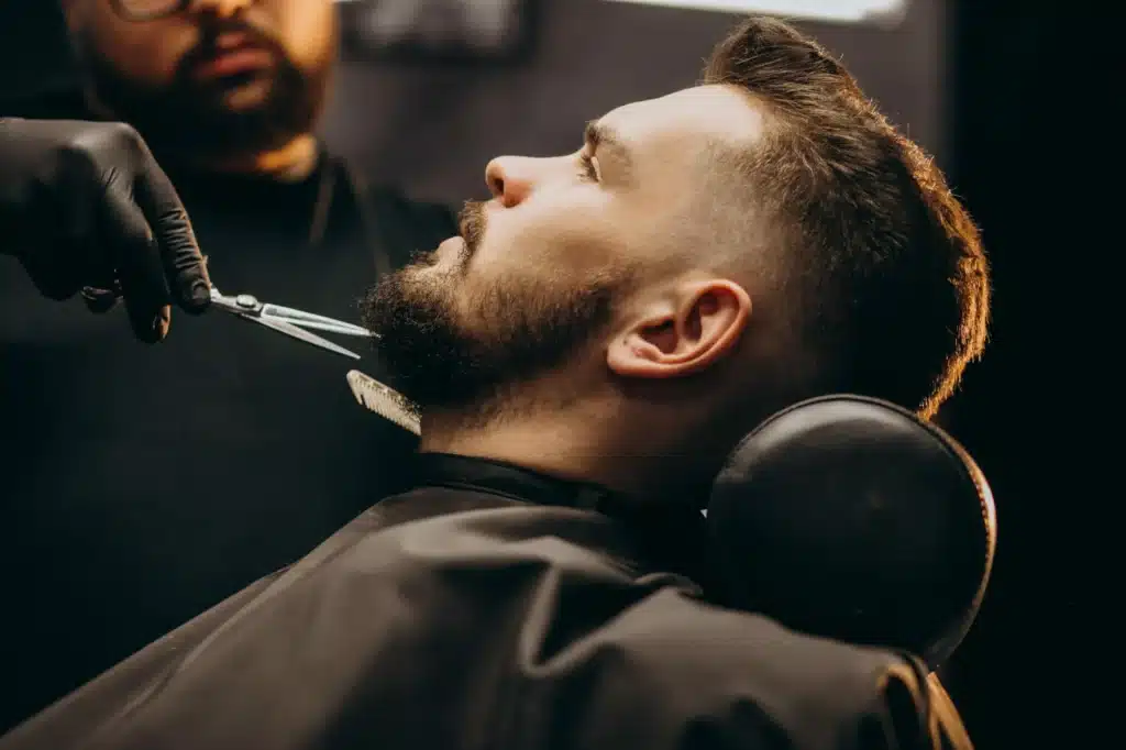 Taille de Barbe Professionnelle au Salon de Coiffure Un coiffeur aux gants noirs taille avec précision la barbe d'un client dans un salon de coiffure tamisé.